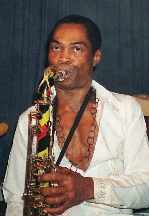 Fela Kuti performing on stage with a trumpet in hand.